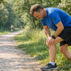 Ein Laeufer mittleren Alters macht eine Pause am Wegrand und greift sich ans Knie